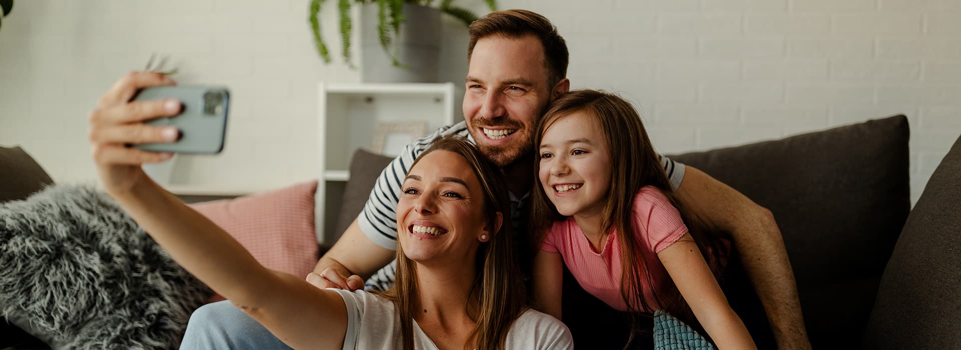 Junge Familie sitzt lächelnd auf dem Sofa in und schießt ein Selfie